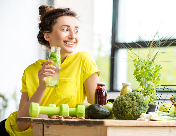 Portrait of a young sports woman in yellow t-shirt sitting indoors with healthy food and dumbbells on the table